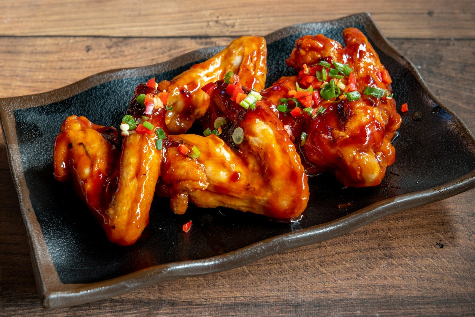 Air fryer chicken wings tossed in sticky sauce on a black plate