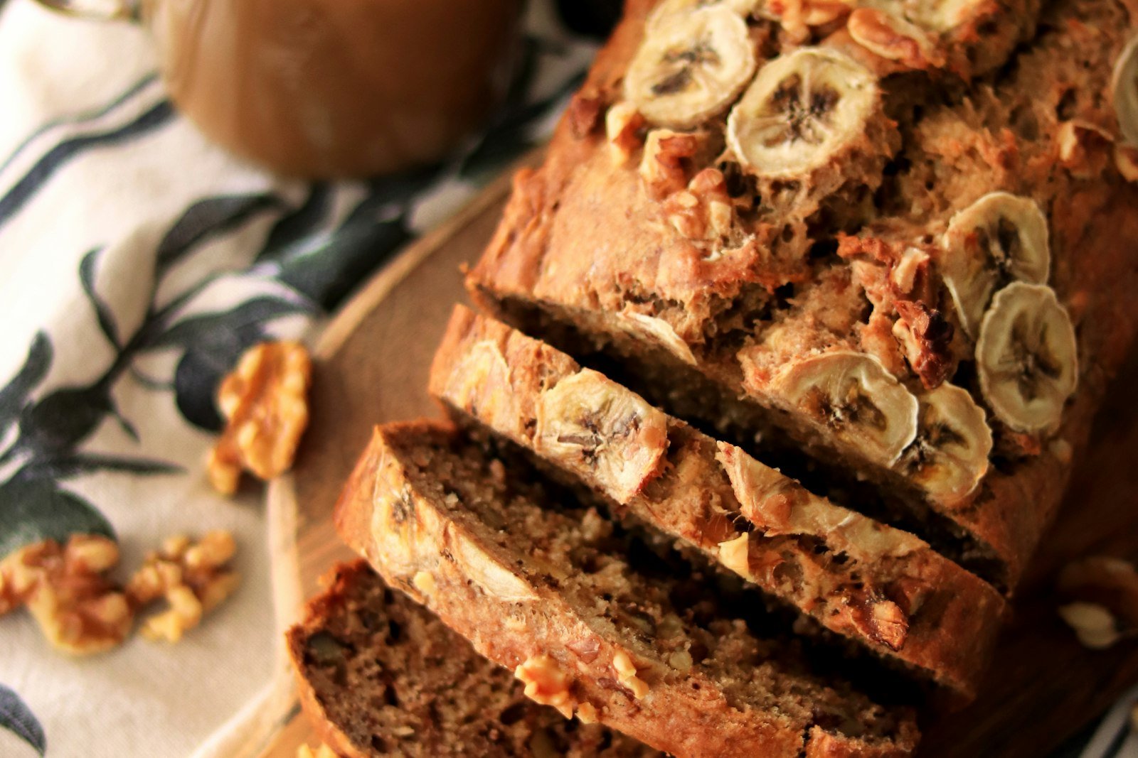 A sliced loaf of banana bread on a wooden board, showing the soft, moist interior and golden crackly crust