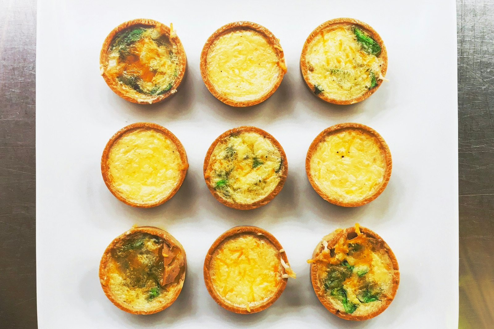 Overhead view of a muffin tin filled with freshly baked egg bites, golden on top and speckled with spinach and red pepper