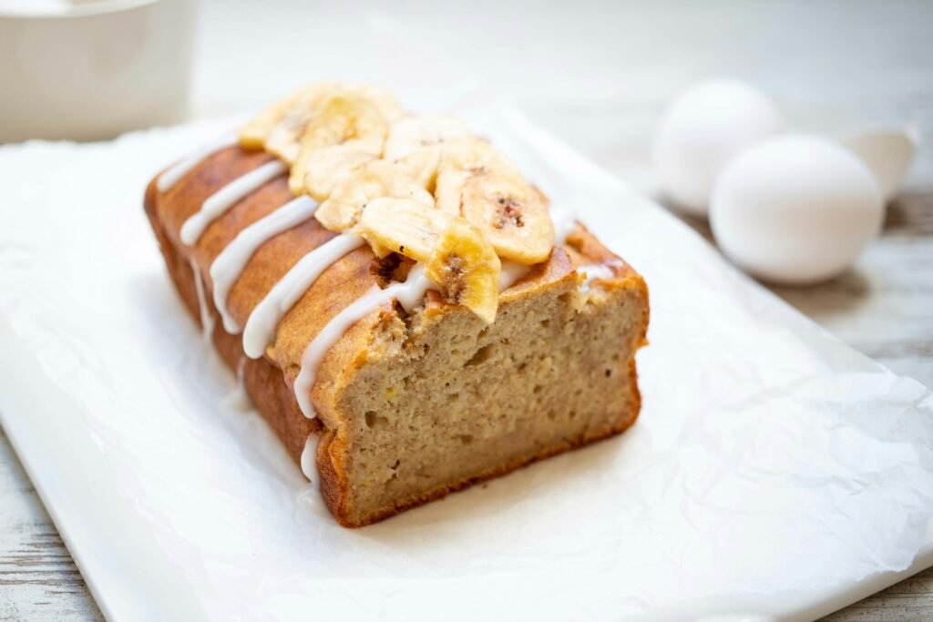 Moist banana bread loaf on a white plate, sliced and ready to serve