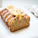 Moist banana bread loaf on a white plate, sliced and ready to serve