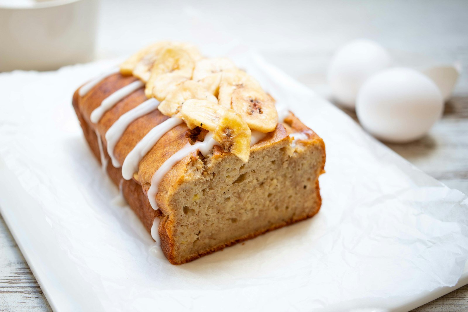 Moist banana bread loaf on a white plate, sliced and ready to serve