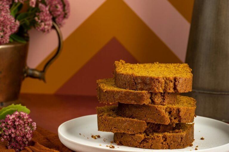 A loaf of moist pumpkin bread with a crackly sugared top, sliced to show the tender, deep orange crumb