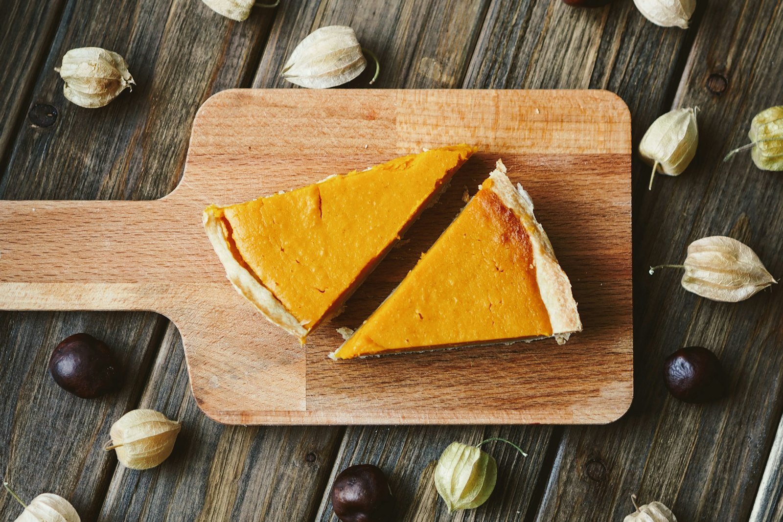 A pan of pumpkin cheesecake bars being lifted out with parchment, showing the smooth orange filling and dark gingersnap crust