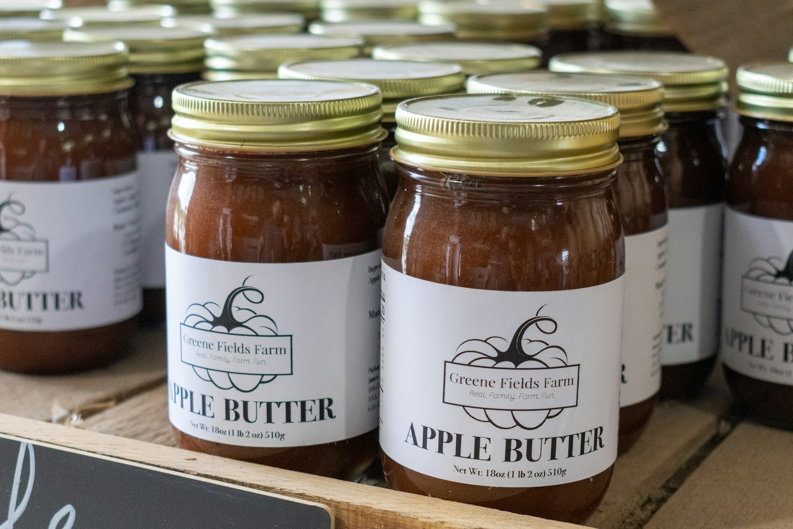 A jar of dark, glossy slow cooker apple butter with a spoon, fresh apples and cinnamon sticks nearby