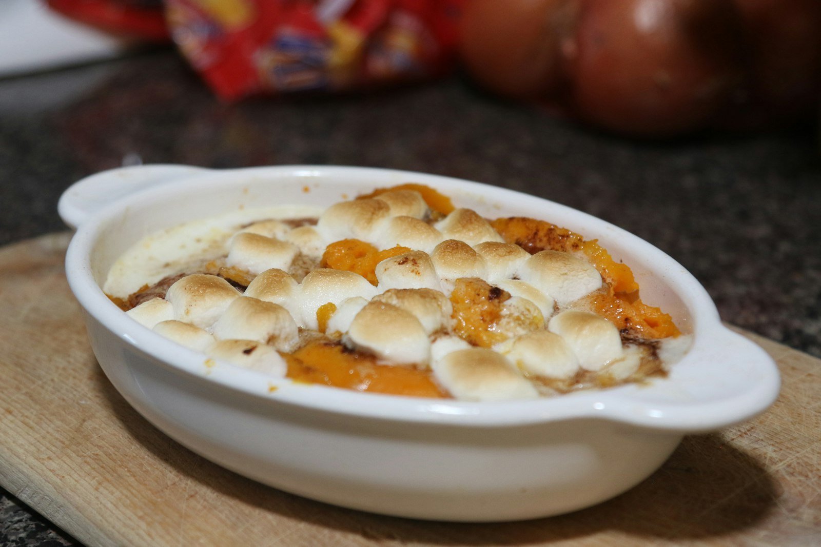 A spoonful of creamy orange sweet potato casserole lifted from the dish, showing gooey toasted marshmallows on top