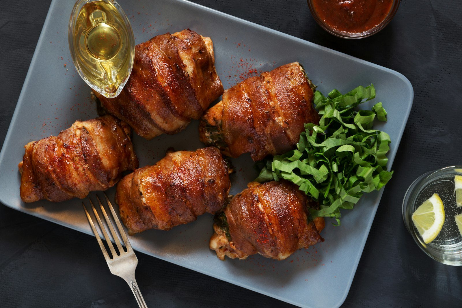 Crispy bacon wrapped dates stuffed with goat cheese, drizzled with maple syrup and sprinkled with thyme, served on a white platter with toothpicks