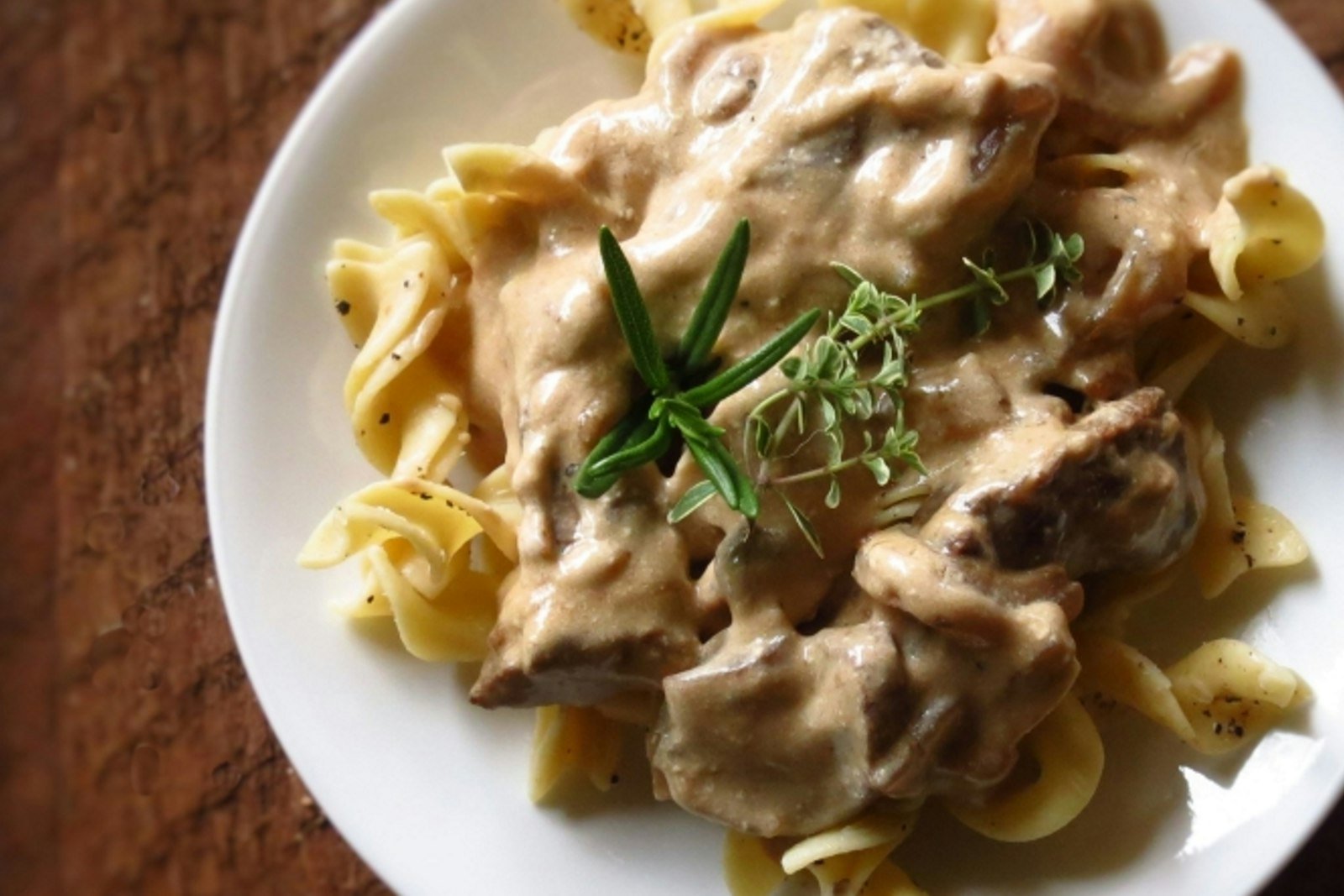 A plate of creamy beef stroganoff with seared steak strips and mushrooms over buttered egg noodles, garnished with parsley