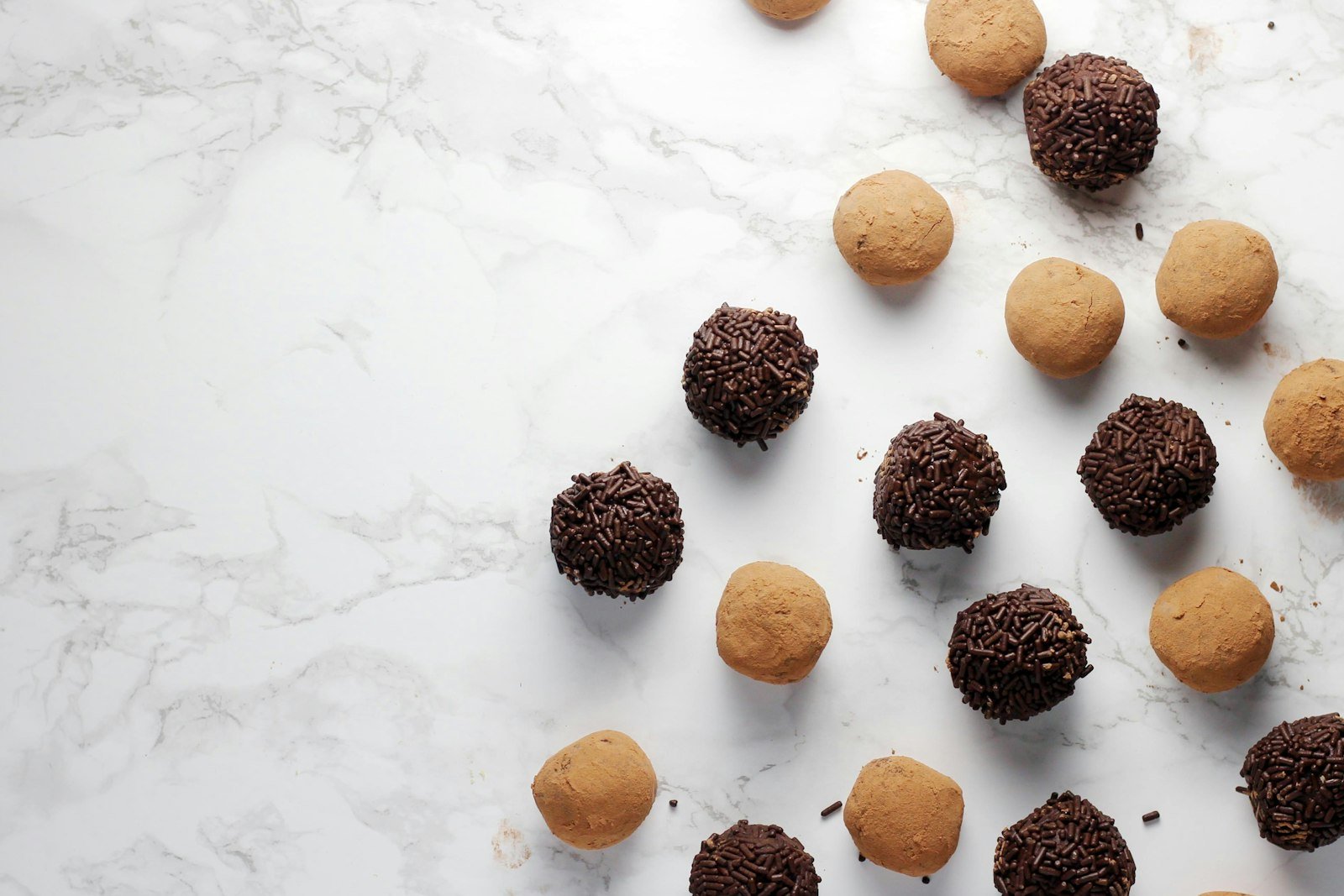 Buckeyes being dipped one at a time into a bowl of melted dark chocolate on toothpicks, with finished candies setting on parchment paper beside the bowl