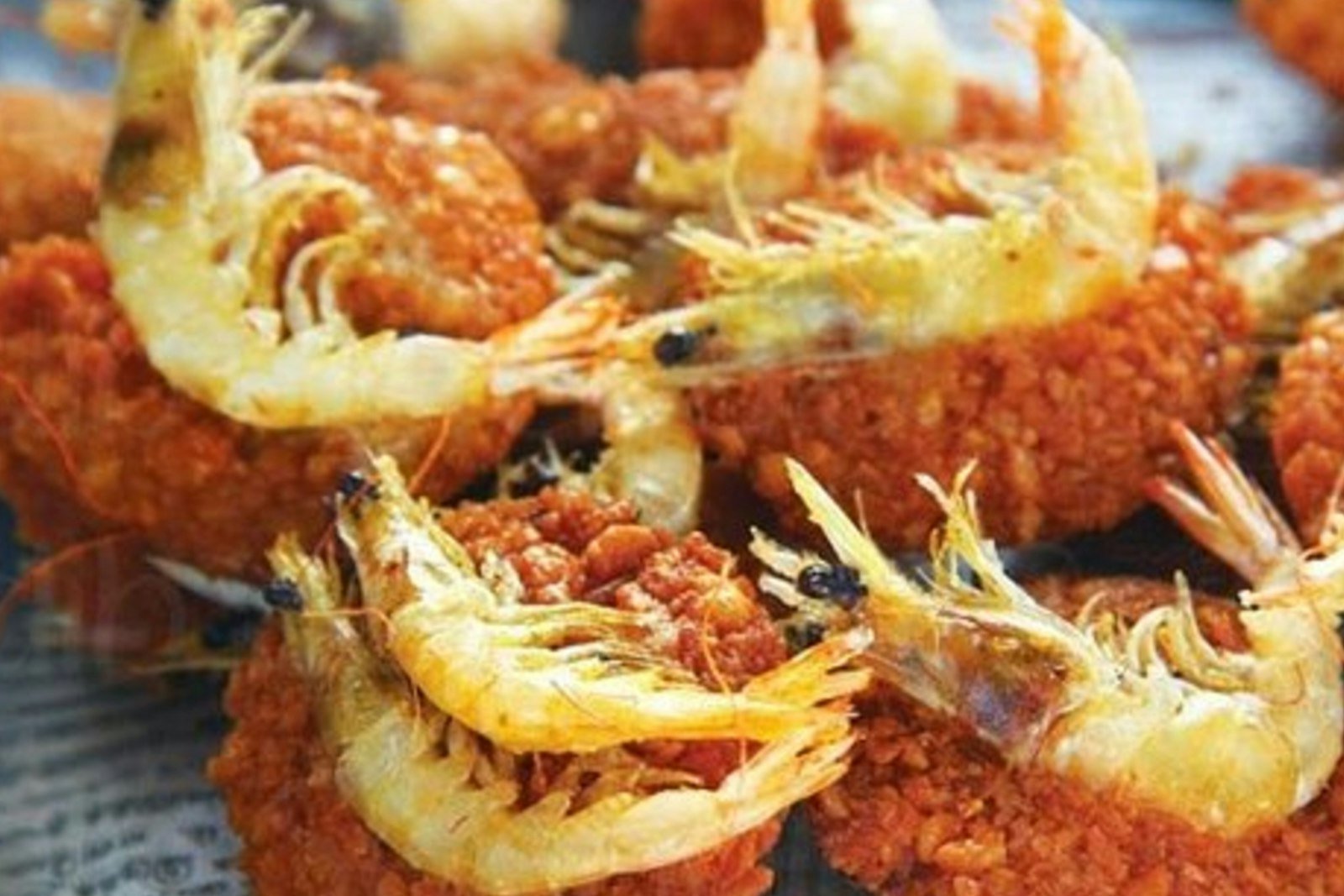 A platter of crispy coconut shrimp with golden, shaggy coconut coating, a bowl of orange chili dipping sauce and lime wedges