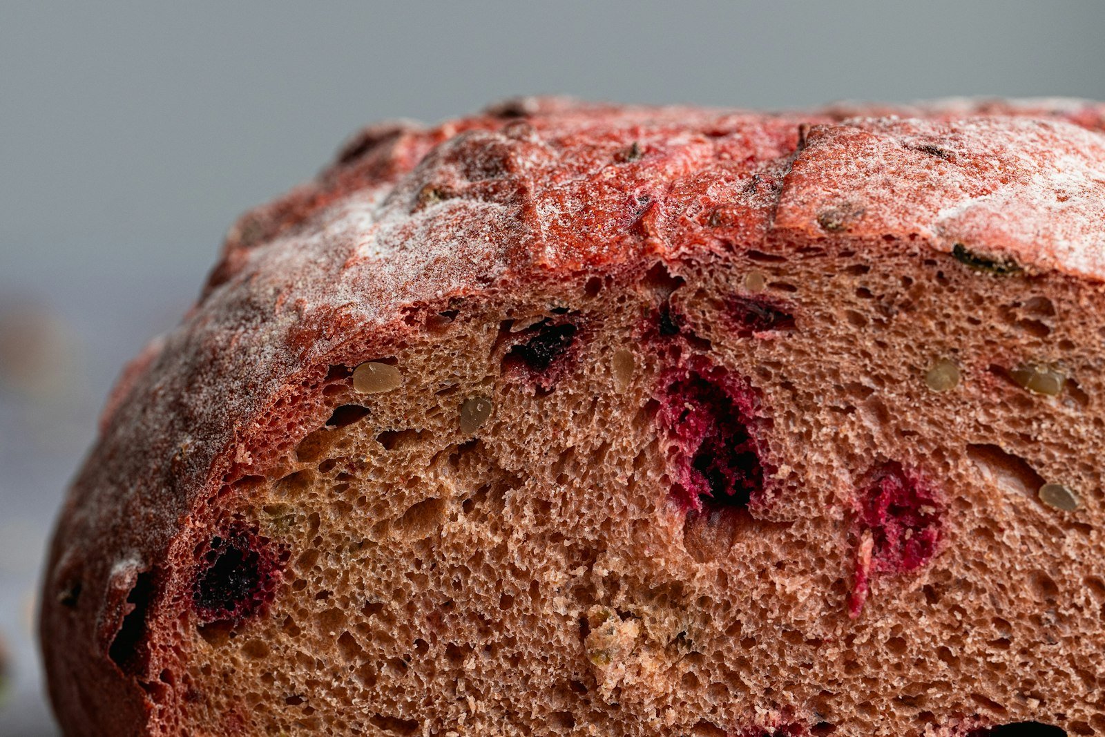 A glazed loaf of cranberry orange bread sliced on a wooden board, showing bright red cranberries in a tender crumb