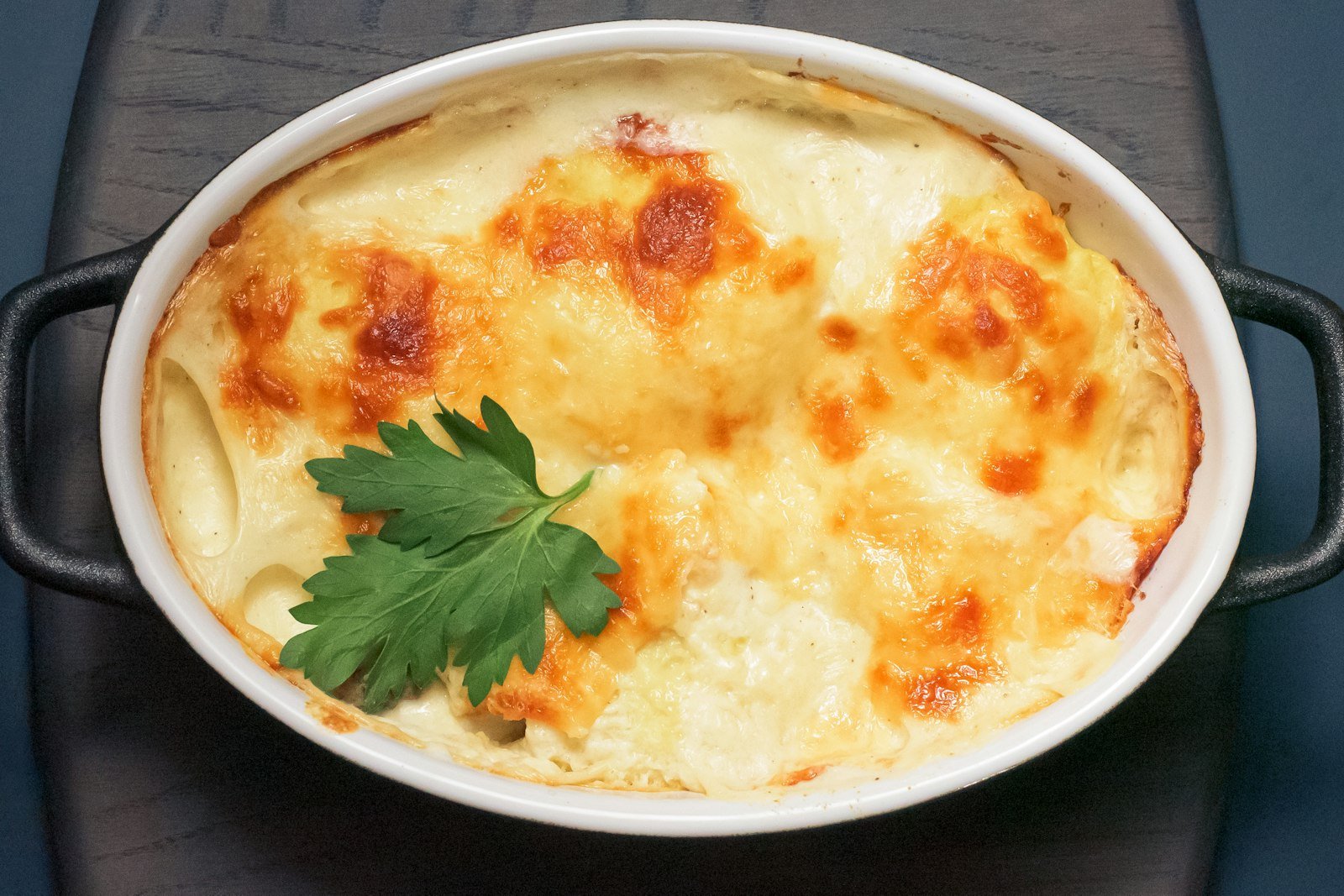 A serving spoon lifting a creamy, cheesy portion of funeral potatoes with a golden cornflake crust out of the baking dish