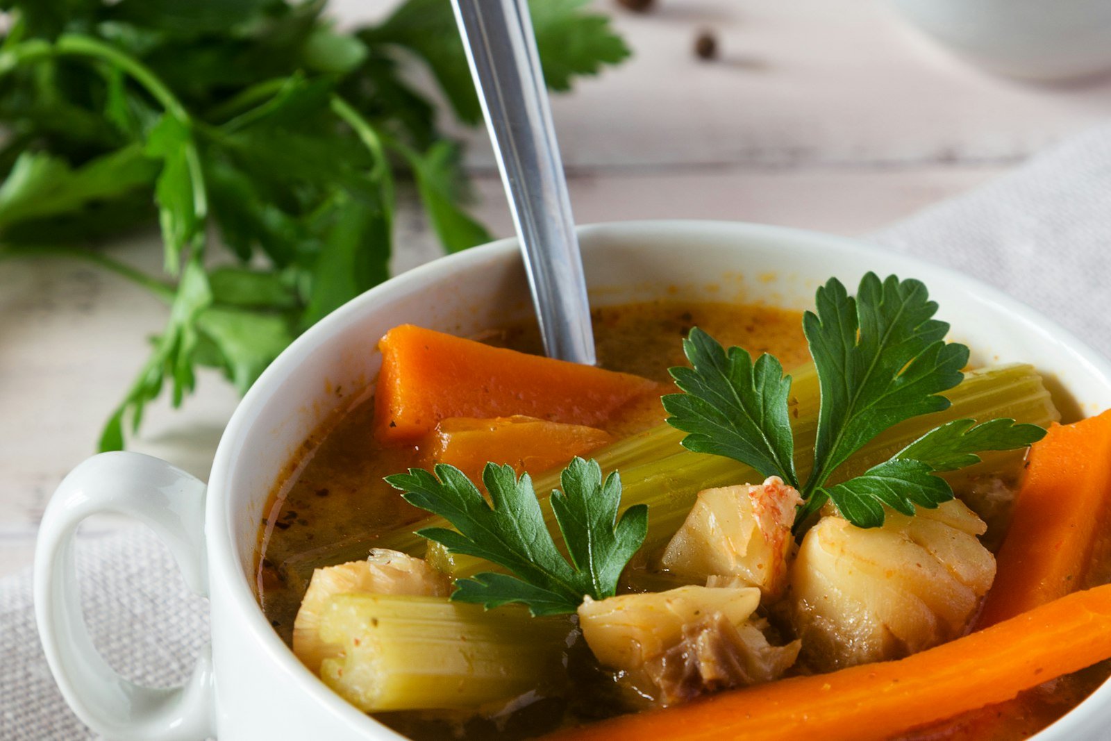 A ladle lifting turkey noodle soup with shredded turkey, egg noodles and sliced carrots out of a blue Dutch oven, with fresh parsley scattered on the counter