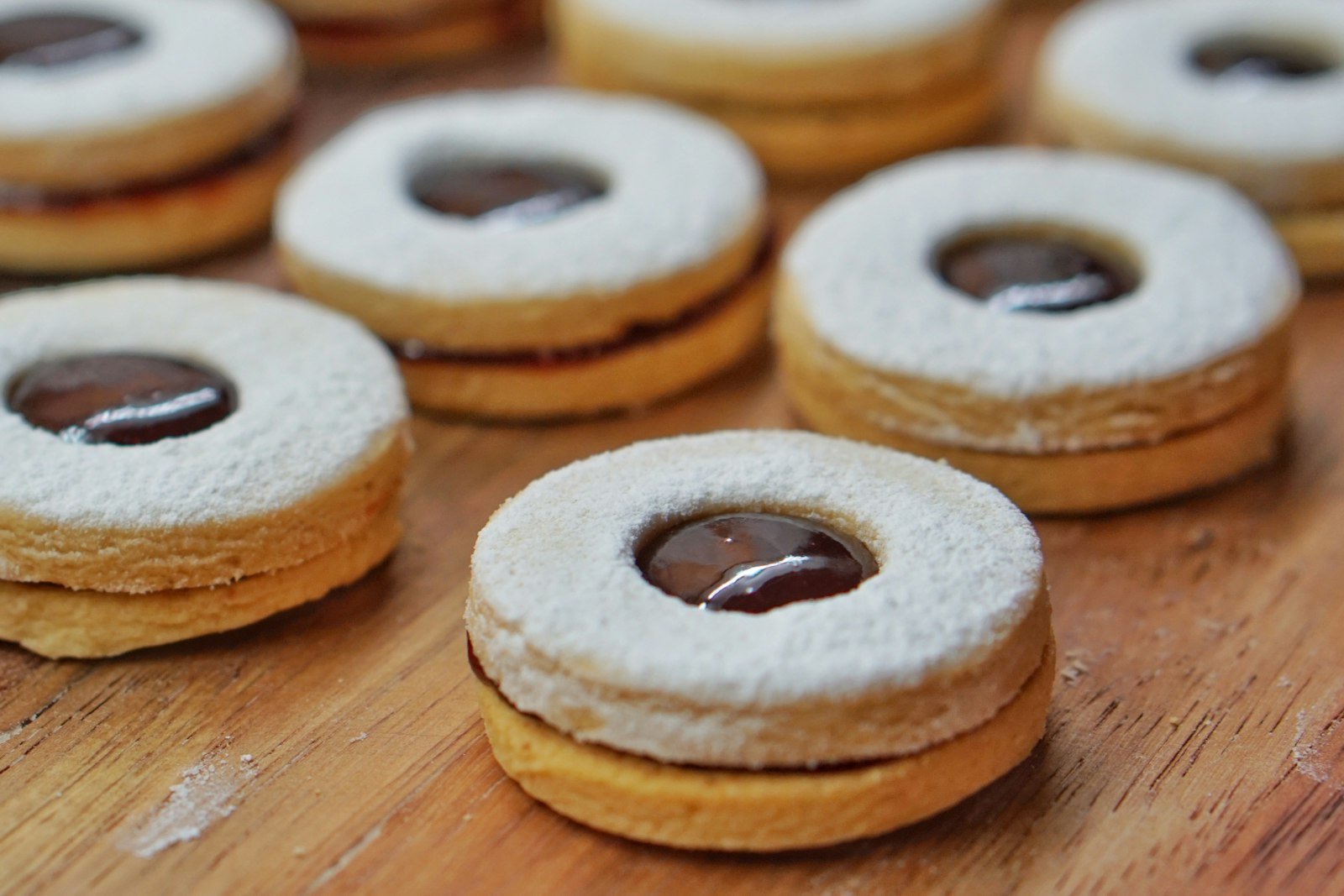 Linzer cookie bottoms spread with raspberry jam next to powdered sugar dusted tops with heart and star cutouts, ready to be sandwiched