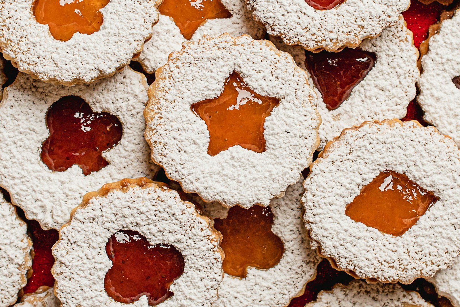 Linzer cookies dusted with powdered sugar with raspberry jam shining through heart and star cutouts on a holiday plate
