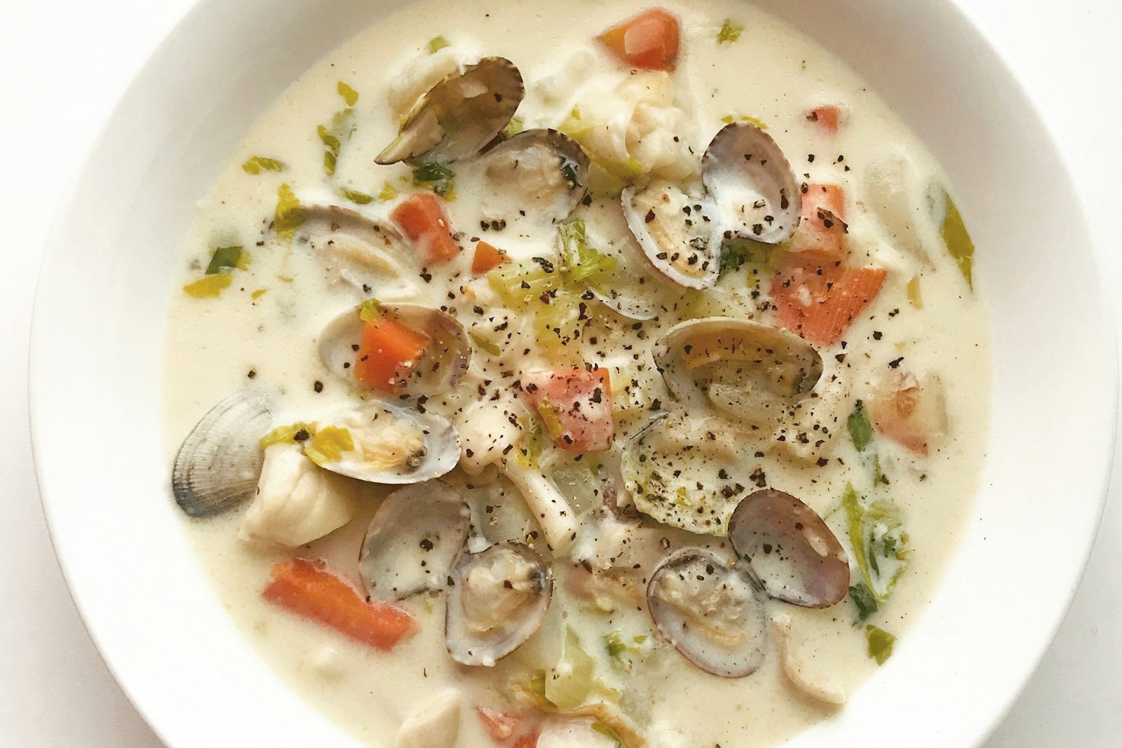 A ladle lifting creamy New England clam chowder with potatoes, clams and crisp bacon from a Dutch oven