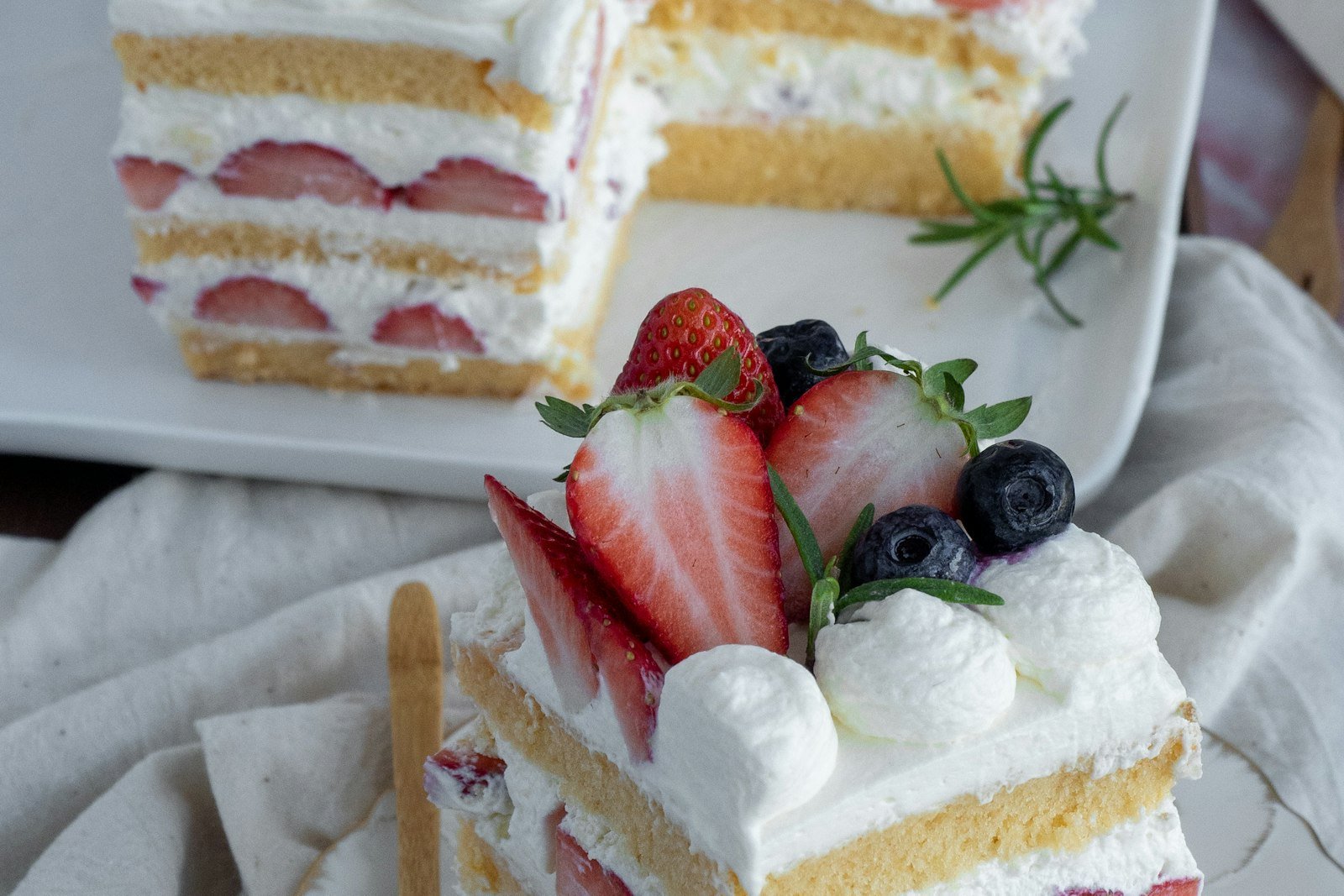 A slice of no-bake strawberry lasagna showing layers of soft graham crackers, whipped cream and fresh strawberries with a pink crunch topping