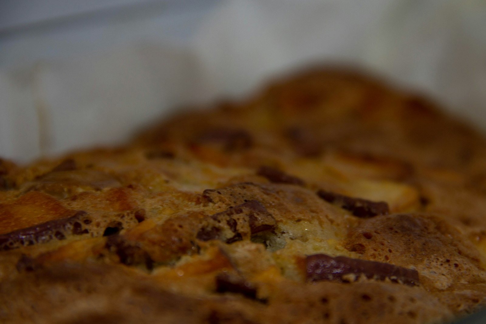A warm square of panettone bread pudding on a dessert plate with vanilla butter sauce pooling around it and a dusting of powdered sugar on top
