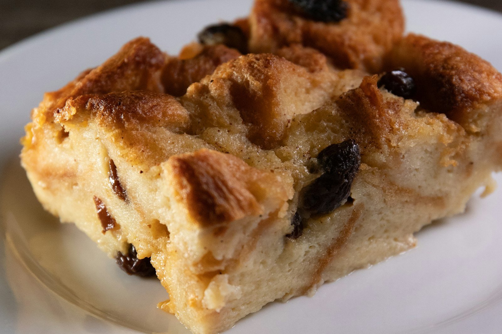 A baking dish of golden panettone bread pudding with crisp, sugared edges, studded with candied orange and raisins, a jug of vanilla sauce beside it