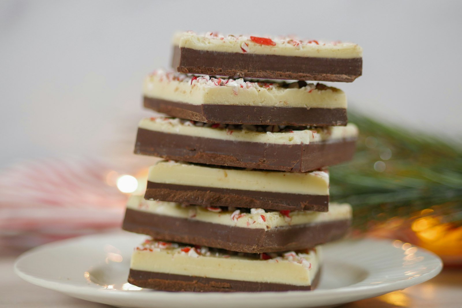 An offset spatula spreading peppermint-scented white chocolate over a set dark chocolate layer in a parchment-lined pan, with crushed candy canes ready nearby