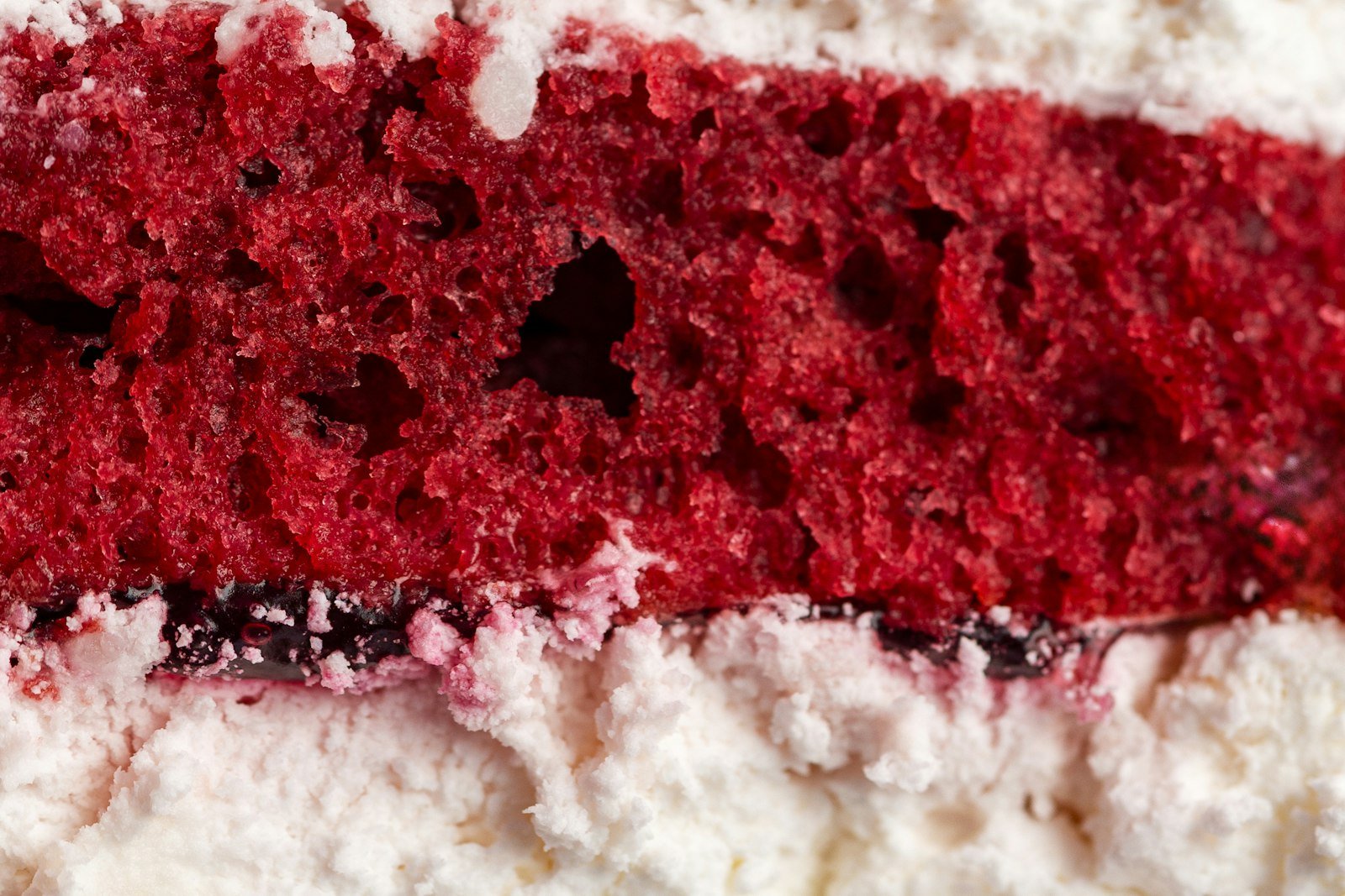 A spoonful of red velvet trifle lifted from the bowl showing moist red cake, fluffy white cheesecake cream and a whole raspberry