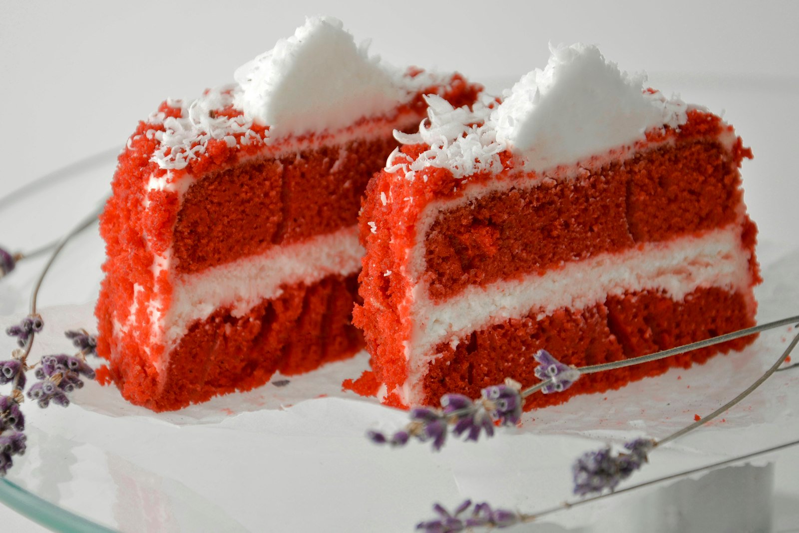 A tall glass trifle bowl filled with layers of red velvet cake cubes, white cheesecake cream and fresh raspberries, topped with cake crumbs and white chocolate curls