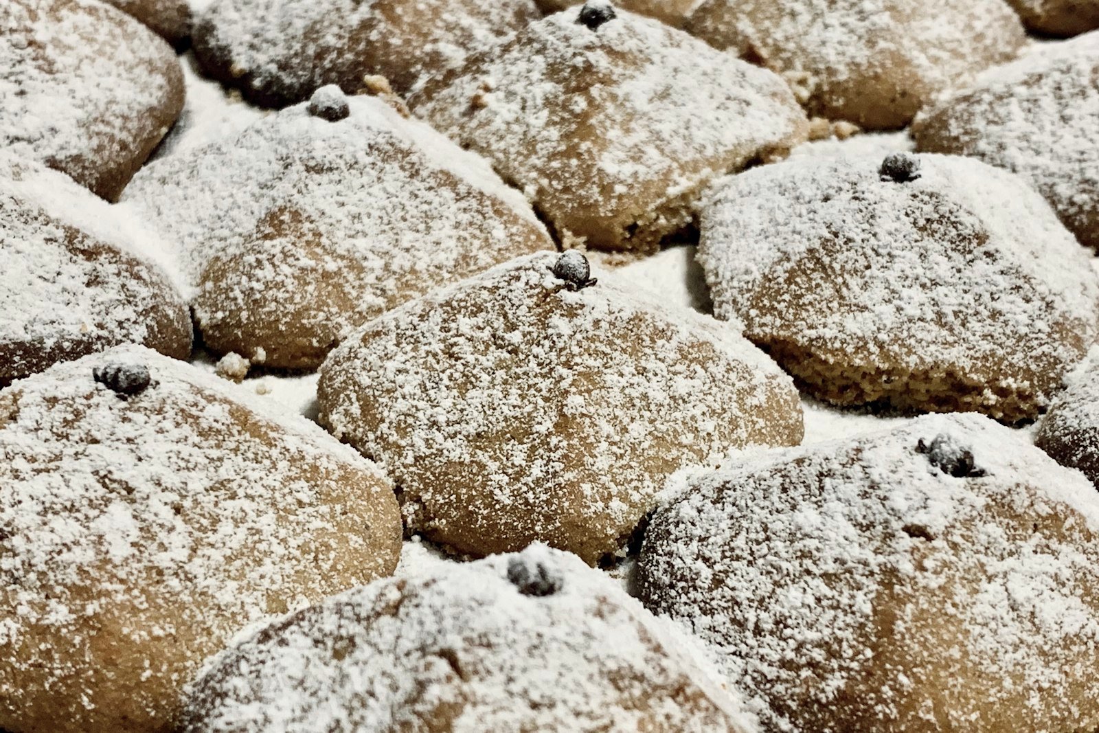 A tray of Russian tea cakes being rolled in a bowl of powdered sugar, with a few finished snowy cookies on a cooling rack