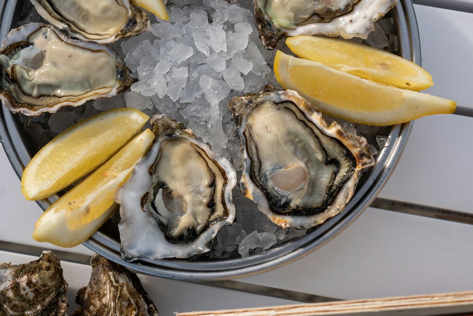 Overhead view of the top tier of a seafood tower with poached shrimp hooked over the rim, chilled mussels, lemon wedges and a small bowl of cocktail sauce nestled in crushed ice