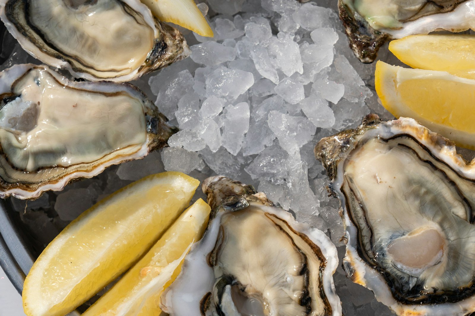 A two-tier seafood tower on crushed ice with shrimp, lobster tails, crab claws, mussels and oysters on the half shell, lemon wedges and three sauces