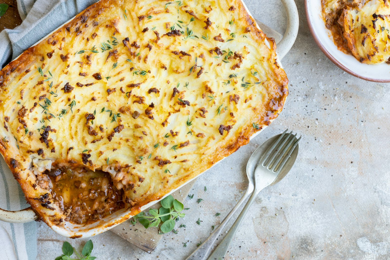 A baking dish of classic shepherds pie with a golden, ridged mashed potato topping, one serving scooped out to show the ground lamb, carrot and pea filling