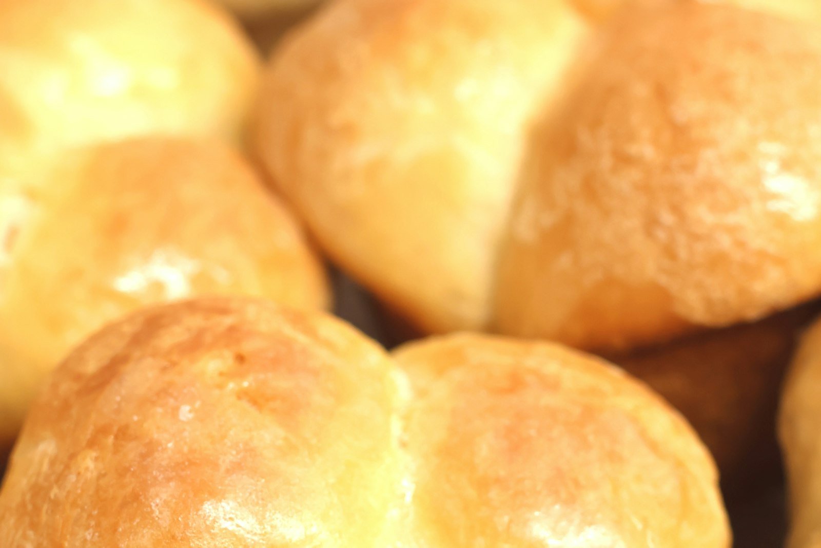 A 9x13 pan of golden, pull-apart soft dinner rolls brushed with melted butter, with one roll torn open to show the fluffy crumb